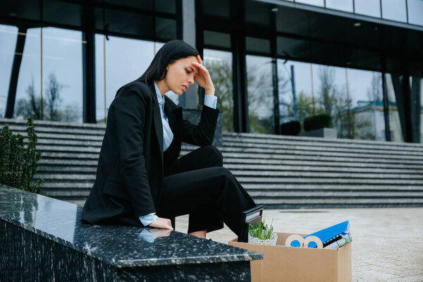 A woman is shown sitting on a cardboard box, holding a sign that reads lost job and looking upset and distressed.