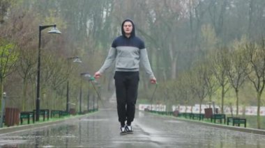 Akrobatik idman atlama halatı yağmurda. Genç bir akrobatik sporcu, dışarıda çalışmak için yağmura göğüs geriyor. Yüksek enerjili bir idman için atlama ipi takıyor..