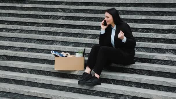 一个紧张的没有工作的人坐在楼梯上 一边用手机说话 有问题的妇女坐在楼梯上 在智能手机上讨论被解雇的工作 — 图库视频影像