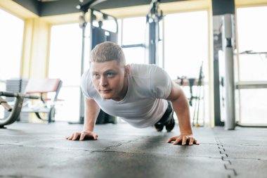 Kararlı bir genç adam yoğun antrenman sırasında iyi donanımlı bir spor salonunda şınav çekiyor. Güçlü ve atletik fiziği, geliştirdiği gücü ve gücü gösteriyor.