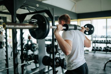 Spor kıyafetleri giyen genç bir adam, yüksek yoğunluklu halter egzersizi yapıyor, aktif ve formda bir yaşam tarzına bağlılığını gösteriyor..