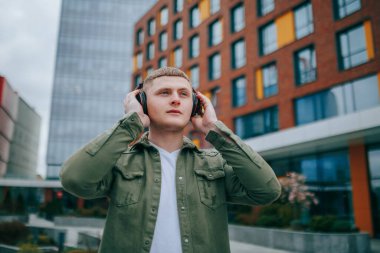 Kulaklıklı, yürüyen ve arkasında şehrin güzel mimarisine hayran olan genç bir çocuk. Melodik Anlar Yakışıklı Adam Şehirde Kulaklıklarının tadını çıkarıyor