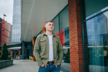 Sarı saçlı Latin bir adam bu modaya uygun portrede genç ve tasasız bir ifadeyle kameraya bakıyor. Kentsel Çevrede Modern Biçim Yakışıklı Erkek