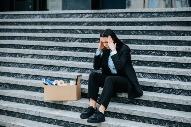 Merdivenlerde oturan bir kadın, düşünceli bir ifadeyle iş kaybının kariyeri ve geleceği üzerindeki etkisini düşünüyor. İş kaybından sonra depresyonda olan esmer kadın dışarıda oturuyor.