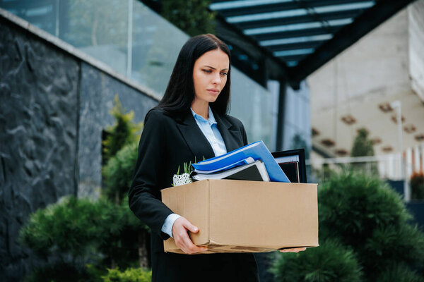 A person standing outside, holding a box, after losing their job and feeling unemployed. Facing the Loss of a Job Woman Outside with Empty Box