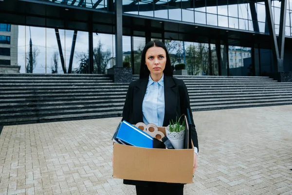 The Struggle of Finding Work After Job Loss. An upset woman holds a cardboard box, facing the uncertainty of job loss and dismissal.