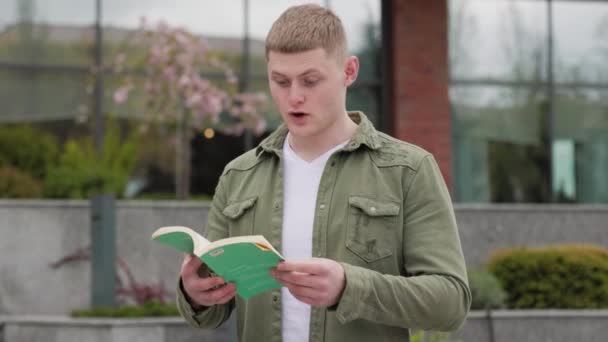 Ένας Όμορφος Άντρας Διαβάζει Ένα Βιβλίο Έξω Ατενίζει Την Απόσταση — Αρχείο Βίντεο