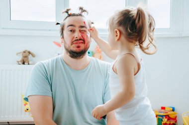Evde komik ve yaratıcı bir makyaj seansının keyfini çıkaran baba ve kız çocuğunun hayal gücünü cesaretlendiriyor. Kahkaha ve ruj Komik bir baba kız anı Sonsuza dek yakalandı