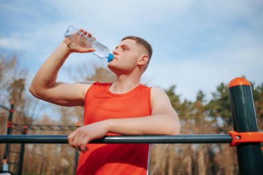 Genç bir sporcunun açık havada su içmesini tazeleyin ve tazeleyin. Genç atletik bir adam spor aktivitelerine ara veriyor ve su içmek için su içiyor..