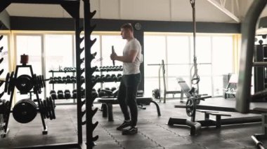 Genç bir adam spor salonundaki halter egzersizinde forma olan bağlılığını ve gücünü gösteriyor. Kararlı bir sporcu, spor salonunda sıkı bir halter antrenmanına katılmış.