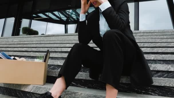 女性は外の階段の上の段ボール箱の上に座り 失業後の仕事のない状況の不確実性と不安を感じている 仕事の損失と階段に座って解雇された女性 — ストック動画