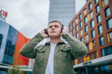 Kulaklıklı yakışıklı bir adam, arka plandaki güzel şehir binalarının manzarasını seyrediyor ve eğleniyor. Şehir Kafiyeli Yakışıklı Adam Kulaklıkla Rahatlıyor