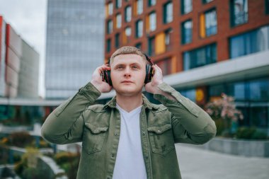 Beyaz gömlekli bir adam, yüksek bir binanın önünde duruyor ve kulaklıkla müzik dinliyor. Şehir Ses Dalgaları Yakışıklı Adam Arka planda Müziğinin tadını çıkarıyor