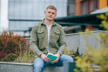 Genç bir adam, dışarıda kitabıyla otururken bir portrede yakalanır. Bu güzel manzara güzel bir zemin görevi görür. Şehirde Kitapla oturan Entelektüel Genç Adam.