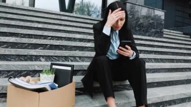 İşsiz bir adam merdivenlerde oturmuş, akıllı telefonuna iş ararken, çaresizce iş arama hüsranı ve işsizlik ararken görülüyor.