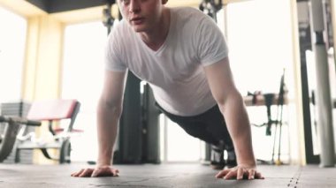 Kararlı bir genç adam yoğun antrenman sırasında iyi donanımlı bir spor salonunda şınav çekiyor. Güçlü ve atletik fiziği, geliştirdiği gücü ve gücü gösteriyor.