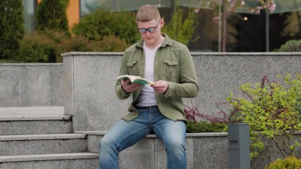 本を読みながら知識を吸収しながら 男学生は屋外で穏やかな午後を楽しんでいます 外の良い本に没頭する男性リーダー — ストック動画