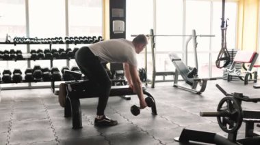 Kendini işine adamış bir erkek sporcu, gücünü ve kararlılığını gösteren titiz bir halter figürü sergiliyor. Enerjik genç adam spor salonunun bir parçası olarak ağırlık kaldırıyor.