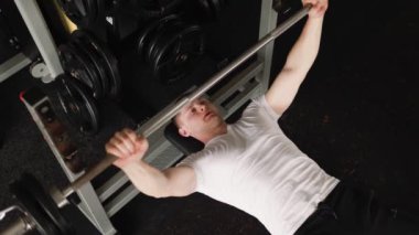 Kararlı genç bir adam spor salonunda halterle yoğun bir egzersiz yapıyor, fiziksel gücü ve dayanıklılığına odaklanıyor. Zincirsiz Adam Spor Salonunda Halterle Egzersiz Yapıyor
