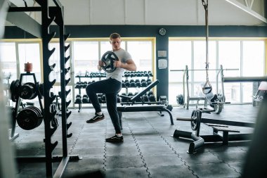 Genç bir adam spor salonundaki halter egzersizinde forma olan bağlılığını ve gücünü gösteriyor. Kararlı bir sporcu, spor salonunda sıkı bir halter antrenmanına katılmış.