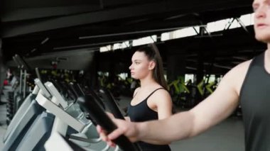 İyi donanımlı bir spor salonunda sağlıklı ve aktif bir yaşam tarzını destekleyen dinamik bir egzersiz sırasında genç bir erkek ve bir kadını eğiten kendini adamış bir fitness eğitmeni..