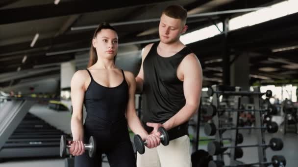 在体育馆里 一位专业的男性私人教练帮助一位女士做哑铃运动 健身指导男私人教练帮助妇女参加健身课 — 图库视频影像