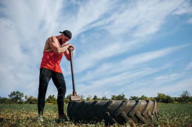 Açık havada çekiçli kaslı adam mola veriyor. Fitness. Kaslı bir adam yoğun bir antrenmandan sonra direksiyonun yanında nefesini tutar..