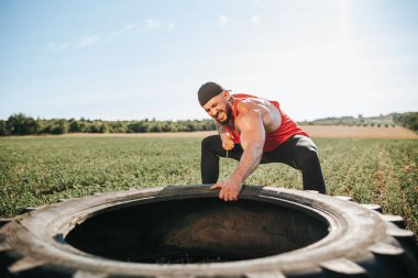 İlham verici bir görüntüde kaslı bir erkek sporcu, fiziksel uygunluk ve kararlılığın bir örneği olarak tekerlek çekme egzersizi yapıyor. Çapraz Fit Hevesli Tekerlek Çekme Eğitimi Dışarıda