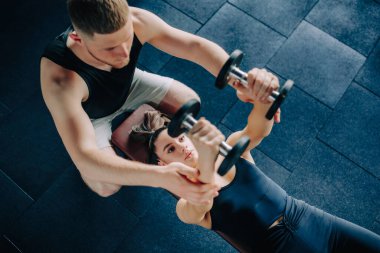 Erkek kişisel antrenörün de desteğiyle bir kadın spor salonunda halterini rahatça kaldırır. Dumbbell Egzersiz Erkek Antrenörü Kadın Antrenmanlarını Destekliyor