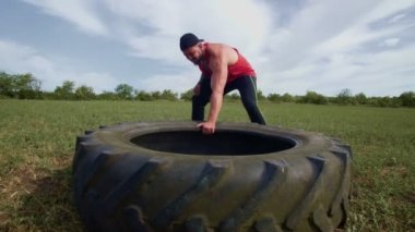 Güçlü bir erkek olarak tanımlanan kendini adamış bir sporcu yoğun bir antrenman sırasında tekerlekleri dışarı çeker. Açık havada Cross Fit Egzersiz Kaslı Adam Tekerleği Çekiyor