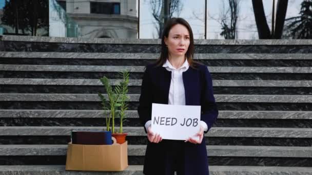 一位中年妇女坐在楼梯上 手里拿着一只印有 需要约伯 字样的纸盒 一面横幅上写着她不高兴的表情和就业的愿望 — 图库视频影像