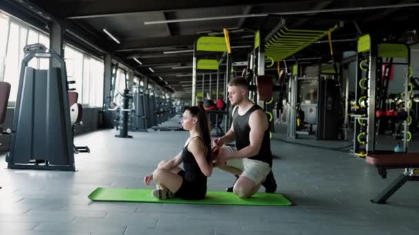 最佳体格健康男按摩师指导妇女在健身房的健身常规 体操馆的专家护理男性理疗师用专门的技巧帮助女性做运动 — 图库视频影像