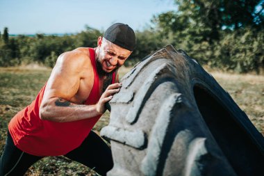 Bu odaklanmış Cross Fit adama açık hava antrenmanında katılın, tekerleği azim ve hassasiyetle kaldırıyor, fitness 'e bağlılığını gösteriyor..