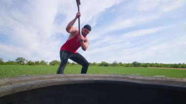 Yavaş kas geliştirme egzersizi. Güçlü adam antrenman sırasında çekiçle lastiğe vurur. Extreme Strength Antrenman Kas Adamı Kauçuk Lastiğe Çapraz Formda Çekiçle Vuruyor