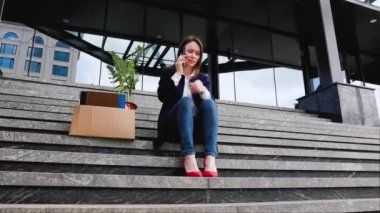 Merdivende oturan bir kadın, gözle görülür şekilde mutsuz, cep telefonuyla iş kaybı ve işten çıkarma hakkında konuşuyor. İşten çıkarıldıktan sonra Smartphone 'da konuşan mutsuz kadın.