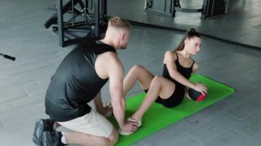 Beyaz bir erkek antrenör, kadın bir müşteriye antrenörlük eğitimi sırasında antrenman topu kullanmak için gerekli teknikleri öğretiyor..