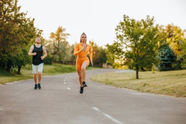 Beyaz tenli bir erkek antrenör, koşu sırasında genç bir bayan sporcuya açık hava egzersizinin önemini vurgulayarak....