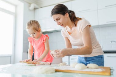 Ev yaratıcılığını kucaklayan genç bir anne ve kızı mutfakta hamur hazırlıyor, aile bağlarını geliştiriyor. Erdemli Aile Anları Anne ve Kız Evde Hamur Hazırlıyor