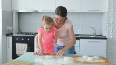 Sıcak ev mutfağında, genç bir anne ve kızı mutlu bir şekilde hamuru hazırlıyor, aile anlarının tadını çıkarıyorlar. Mutfak Maceraları Anne ve Kızının Evcil Zevki