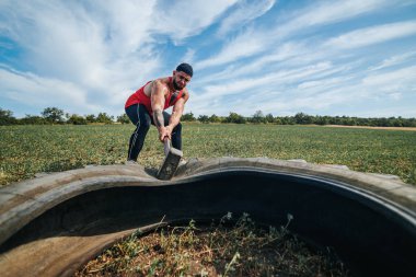 Kas Geliştirme Egzersizi Güçlü Adam Çapraz Antrenman sırasında Çekiçle Tekere Vuruyor. Extreme Strength Antrenman Kas Adamı Kauçuk Lastiğe Çapraz Formda Çekiçle Vuruyor