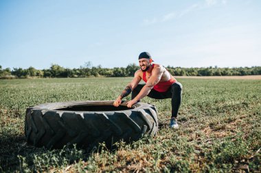 Açık havada Cross Fit antrenmanına katılan Amerikalı bir sporcu, tekerlek çekme egzersizi yaparken kaslı fiziğini sergiliyor. Çapraz Fit Eğitiminde Kaslı Adam Tekerleği Dışarı Çekiyor