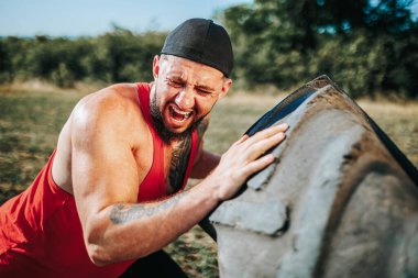 Zorlu bir açık havada, Cross Fit rutininin ortasında, bu kaslı adam kendine güvenen ve güçlü bir tekerleği kaldırıyor, fiziksel uygunluğa olan bağlılığını gösteriyor..