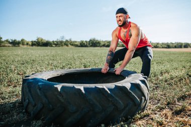 Güçlü bir erkek olarak tanımlanan kendini işine adamış bir Cross Fit sporcusu yoğun bir antrenman sırasında tekerlek çekerek dışarı çıkıyor. Açık havada Cross Fit Egzersiz Kaslı Adam Tekerleği Çekiyor