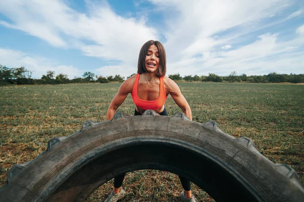 A determined Cross Fit woman working out and lifting a wheel during her outdoor fitness routine. Outdoor Cross Fit Exercise Female Athlete Working Out with a Wheel