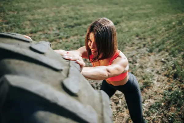 Strong and fit woman lifting a wheel during her outdoor training session. Determined Woman Pushing Her Limits with a Wheel Lift