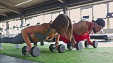 Hareketli bir spor salonunda, bir grup kararlı sporcu, hem erkek hem de kadın sporcular, halterli antrenman yapıyorlar, spor yapmaya bağlılıklarını gösteriyorlar..