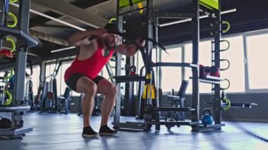 Konsantre ve kararlı bir genç adam halat egzersizini kapalı spor salonunda yapıyor. Kaslı fiziği, kendini adamışlığı ve atletizmiyle birleşmiş.,
