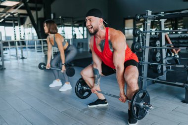 İspanyol bir kadın ve Amerikalı bir erkek spor salonunda halter ile halter çalışırlar, fiziksel zindelik ve güç eğitimine bağlılıklarını gösterirler..