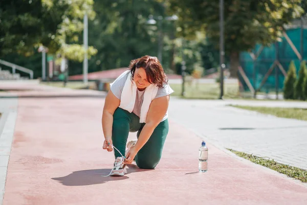 An overweight woman ties his shoelaces is determined to improve her healthy lifestyle through outdoor exercise. Determination in Action Overweight Womans Outdoor Workout for Weight Loss