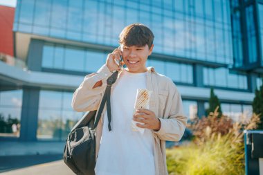 Açık hava sohbetleri, Asyalı Koreli gülen öğrenci, akıllı telefonuyla konuşurken gülen ve hareket halinde yemek yiyen adam. Bir telefon görüşmesi ve atıştırmalıkla meşgul.